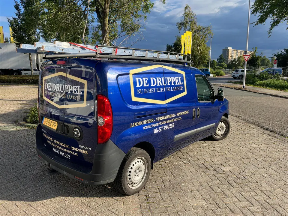 De blauwe bestelbus van De Druppel met het gouden logo en de regel Loodgieter · Verwarming · Zinkwerk